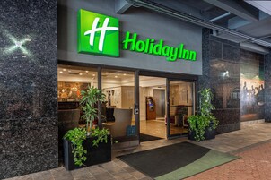 The exterior of a Holiday Inn hotel with a prominent green logo, large glass doors, and potted plants at the entrance.