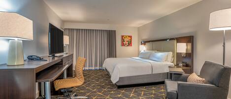 A hotel room with a bed, desk, chair, and a large window with curtains.