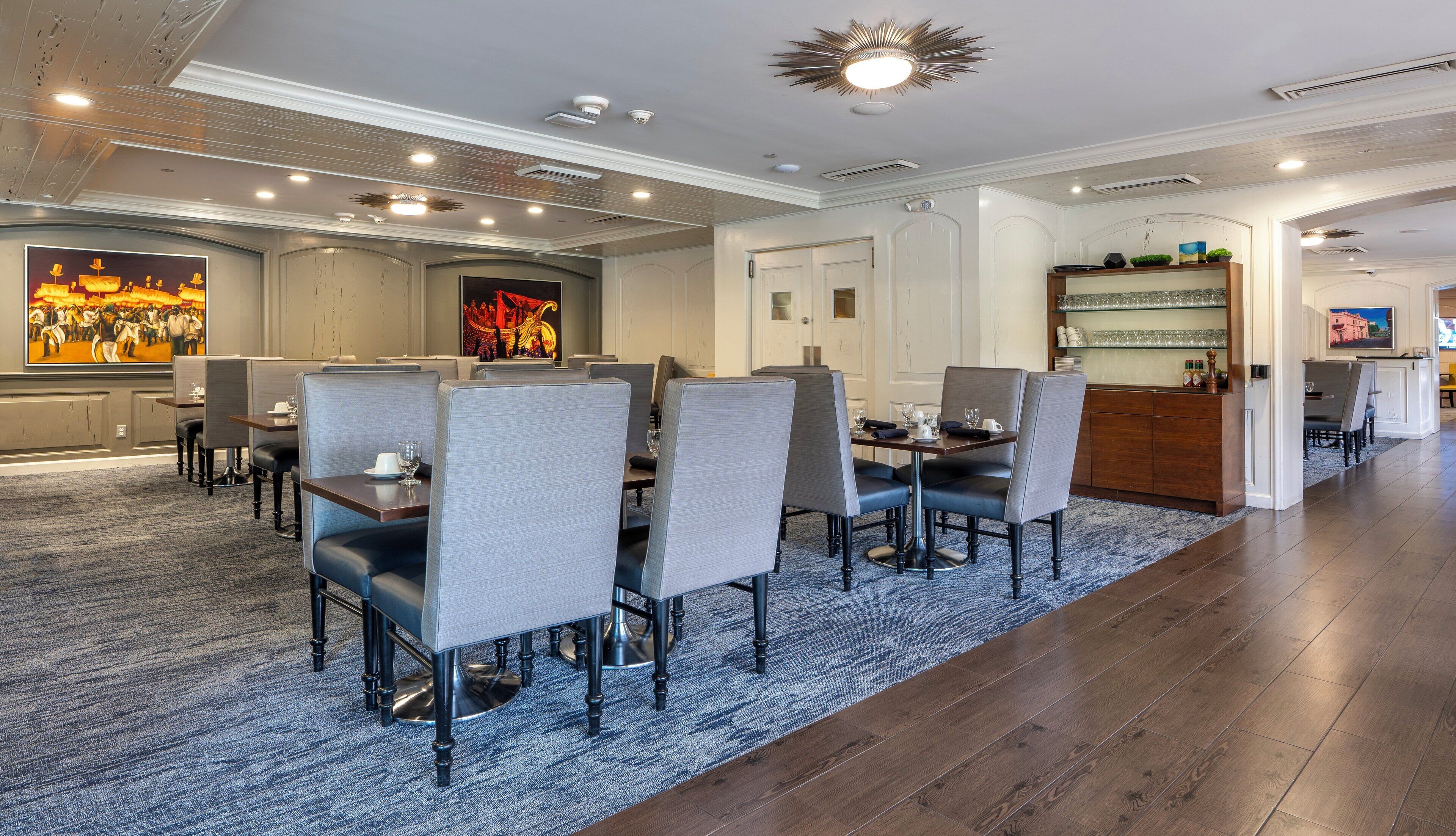 A hotel dining area with a long table, multiple chairs, and a bar area with a television.