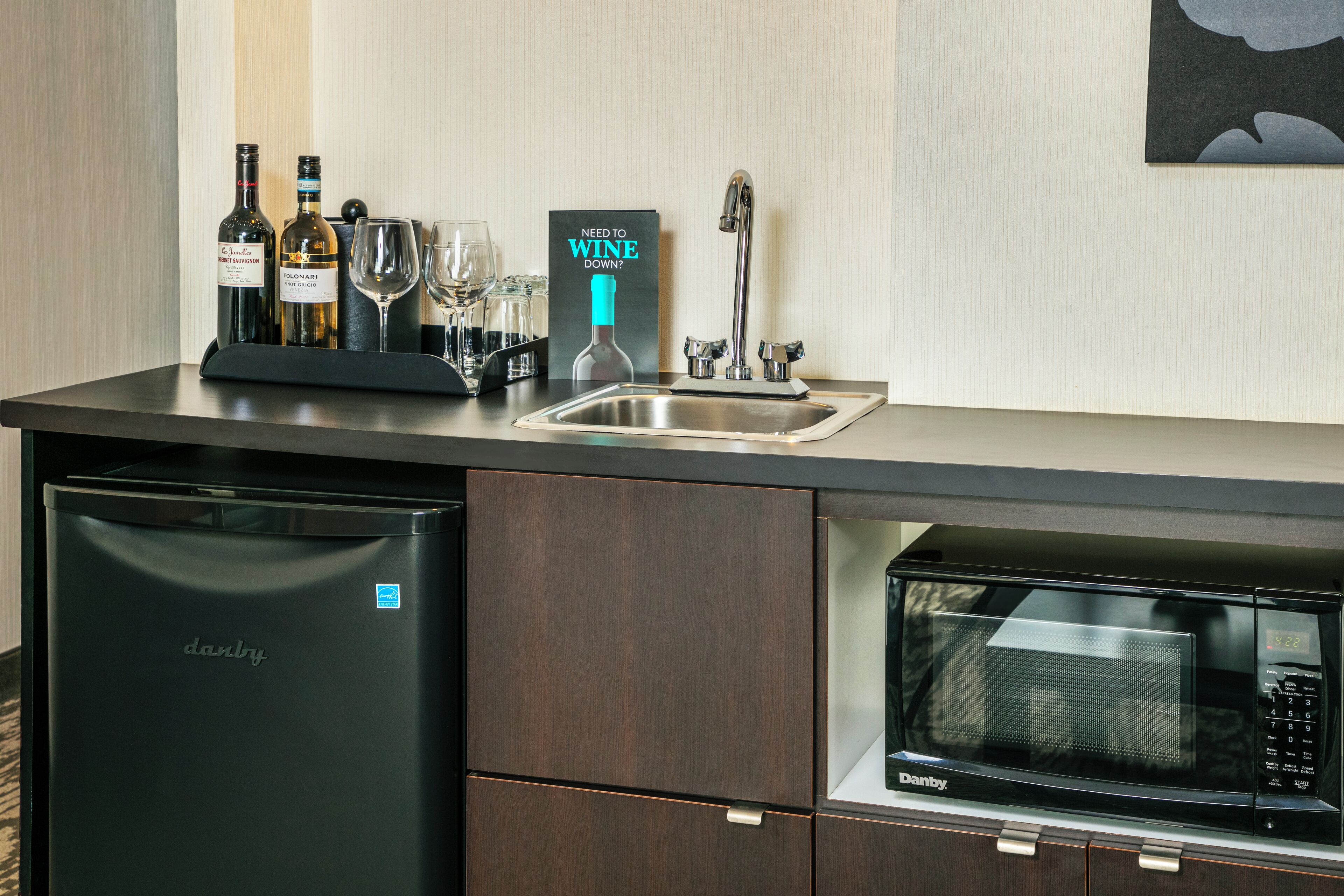 A kitchen with a dishwasher, a microwave, a wine cooler, and a wine bottle.
