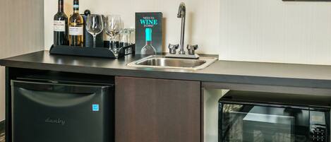 A kitchen with a dishwasher, a microwave, a wine cooler, and a wine bottle.