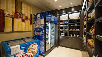 A self-service ice cream machine with a drumstick flavor, a refrigerated display case, and shelves stocked with snacks and beverages.