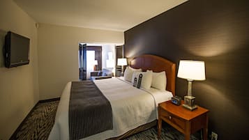 A hotel room with a large bed, a bedside table with a lamp, and a flat-screen TV mounted on the wall.
