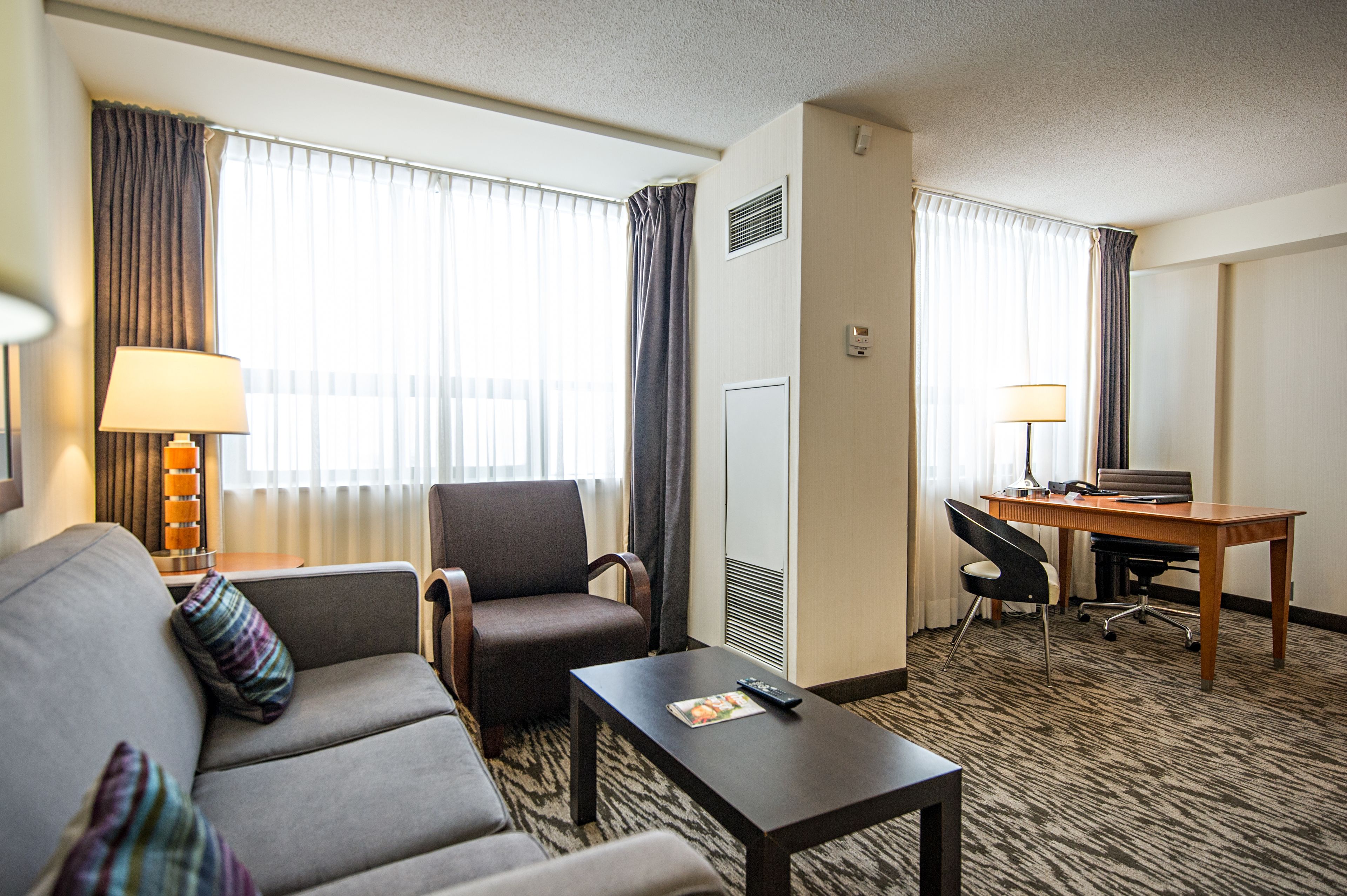Habitación de hotel con sofá, sillón, pequeña mesa y escritorio con silla.