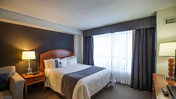 Une chambre d’hôtel avec un grand lit, une table de chevet avec une lampe, un bureau avec une chaise et une fenêtre avec des rideaux.