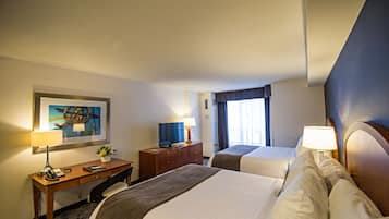 Habitación de hotel con dos camas, un escritorio con lámpara, un televisor y un cuadro en la pared.