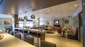 A modern restaurant with a long counter, multiple seating areas, and pendant lighting. - Cambridge Suites Hotel (Halifax)