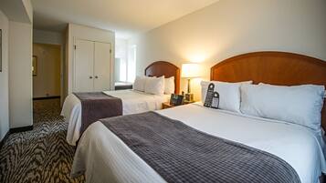 A hotel room with two beds, a desk, a lamp, and a wardrobe.