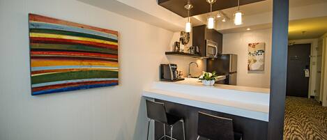 A modern kitchen with a white countertop, stainless steel appliances, and a colorful abstract painting on the wall.
