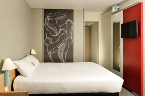 A hotel room with a bed, two bedside lamps, a wall-mounted TV, and a large abstract artwork. - Hotel ibis Nemours (Nemours)