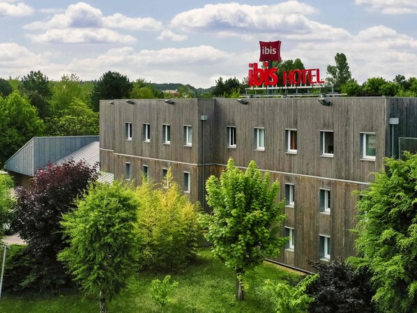 Un moderno edificio de hotel con un llamativo letrero 'ibis', numerosas ventanas y rodeado de vegetación.