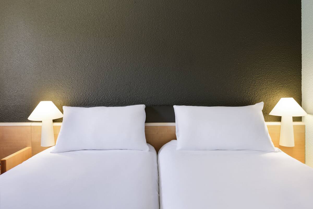 A double bed with white linens, two bedside lamps, and a textured dark wall.