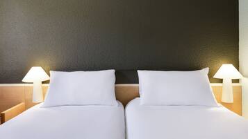 Una cama doble con sábanas blancas, dos lámparas de noche y una pared oscura con textura.