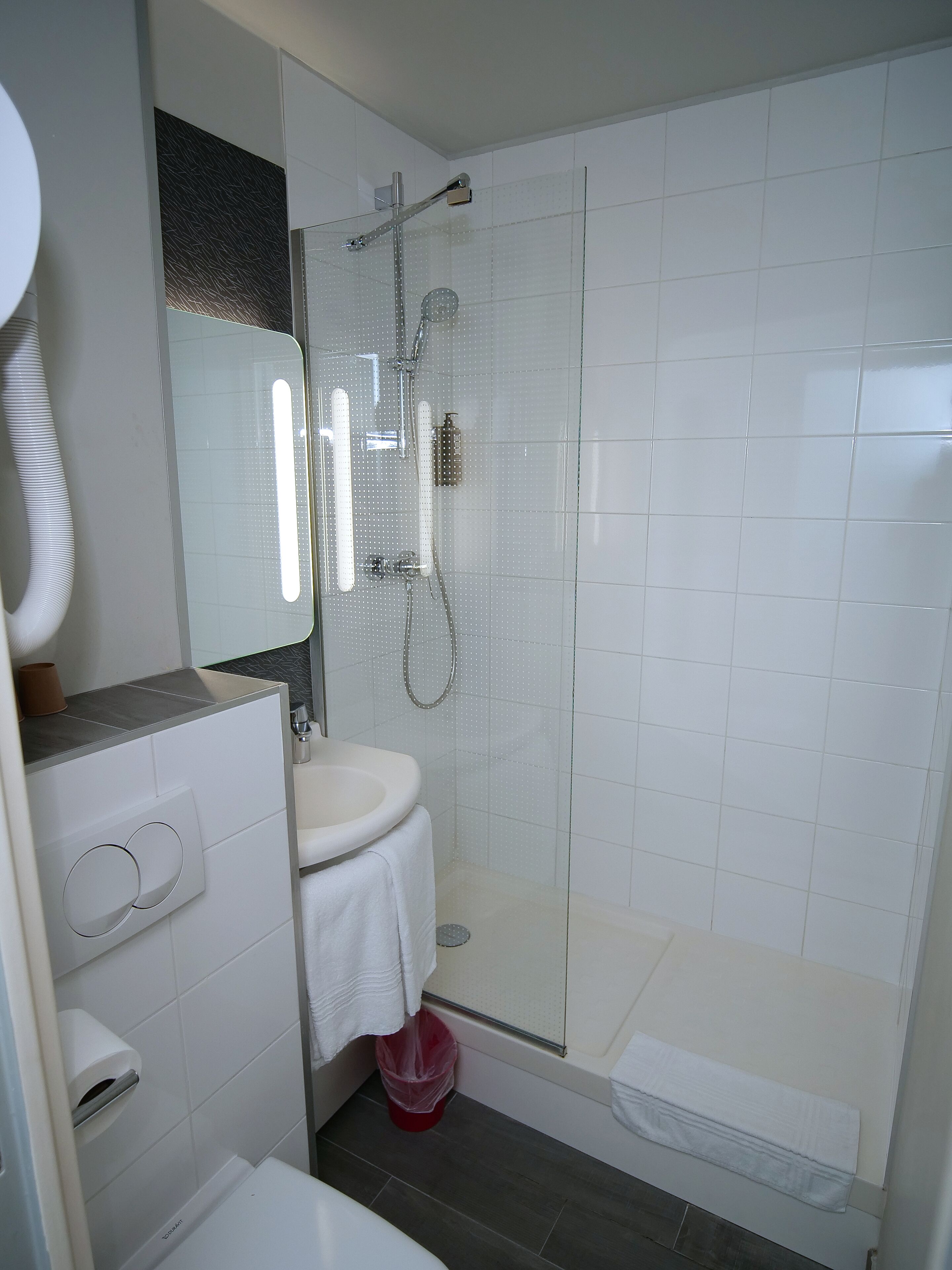 Un baño moderno con ducha de vidrio, lavamanos blanco y retrete.