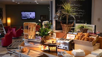 A breakfast buffet with various food items, a chalkboard with menu items, and a television in the background.
