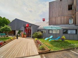 Un edificio moderno con una terraza de madera, una entrada roja y un paraguas azul.