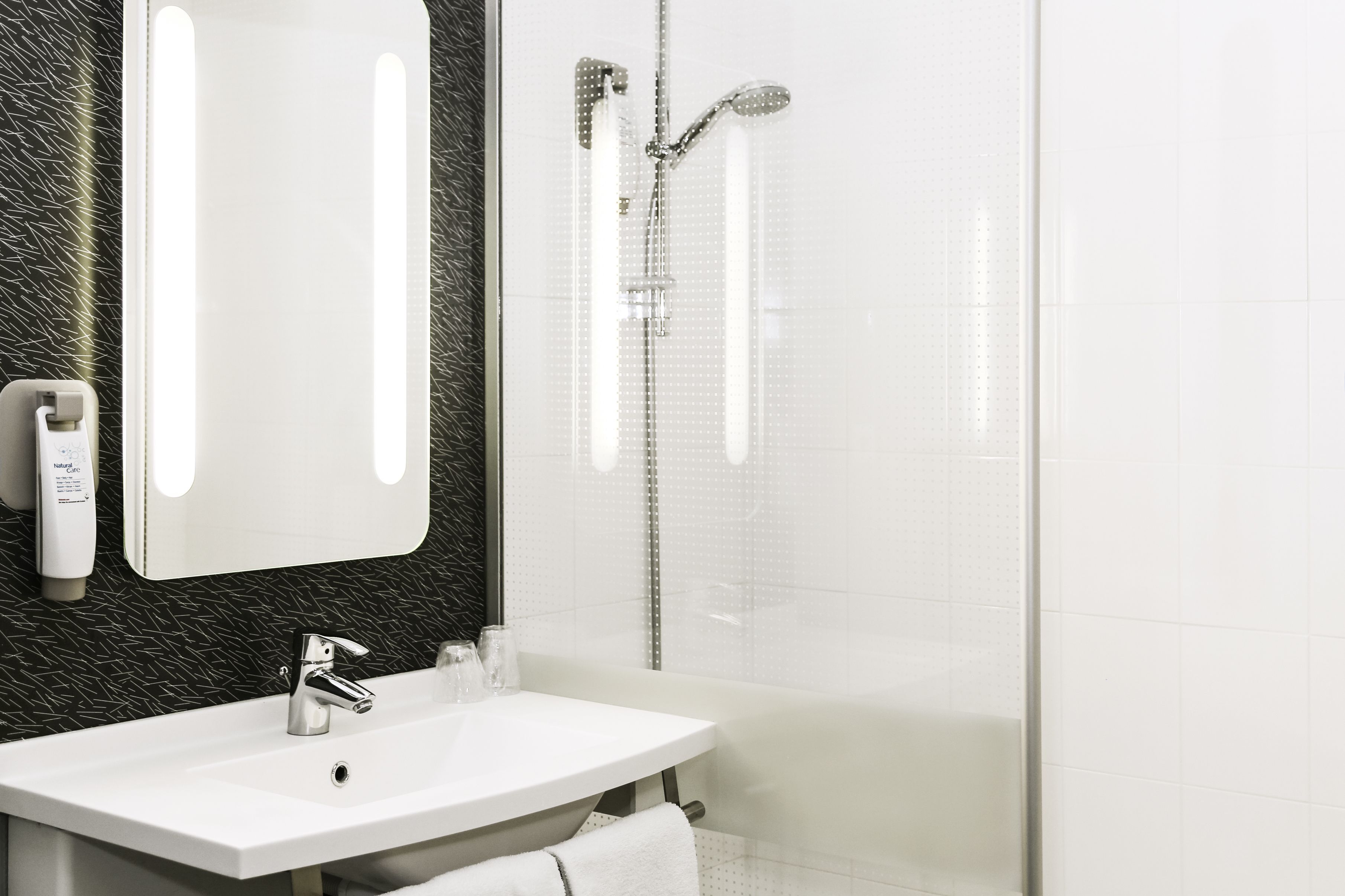 A modern bathroom with a white sink, a mirror, a handheld showerhead, and a glass-enclosed shower.