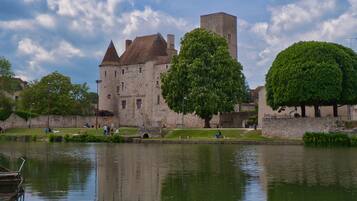 A historic stone building with a moat, surrounded by lush greenery and a calm water body.