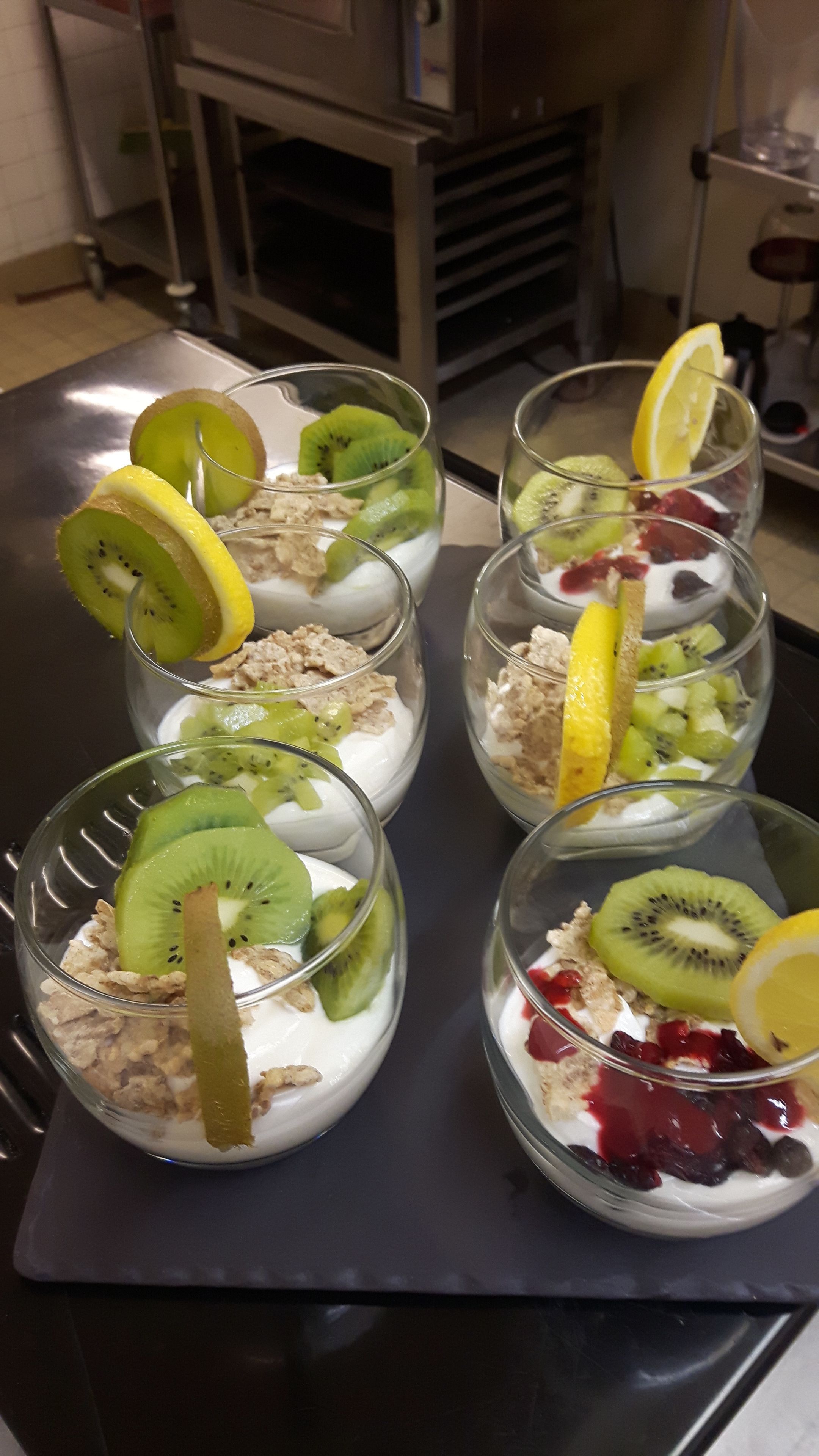 Una mesa con seis recipientes de vidrio que contienen un postre de frutas y granola.