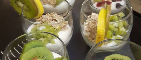 Una mesa con seis recipientes de vidrio que contienen un postre de frutas y granola.
