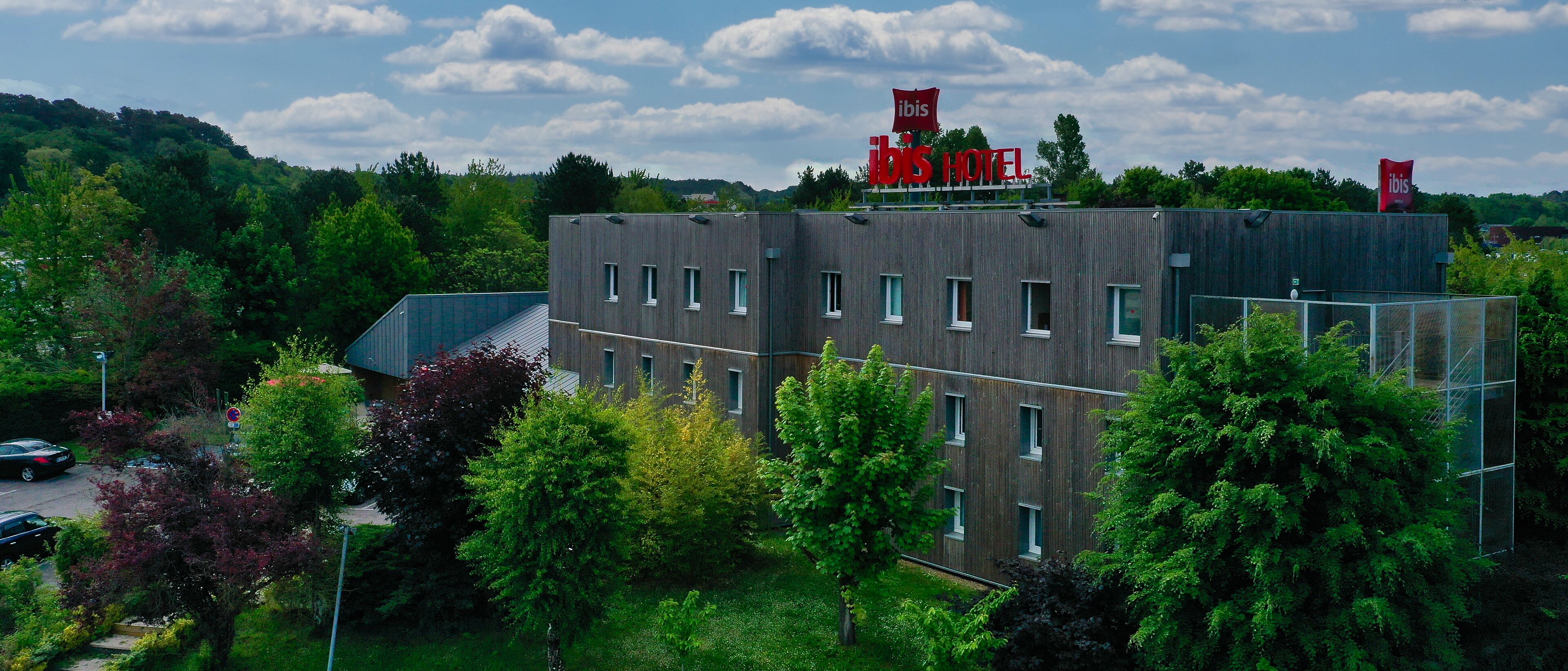 Un hotel moderno con techo plano, múltiples ventanas y un letrero que dice 'ibis HOTEL' en la parte superior.