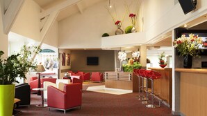 Un vestíbulo de hotel con asientos rojos, una recepción y un televisor montado en la pared.