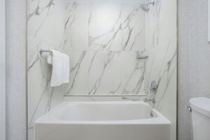A modern bathroom with a marble wall, a bathtub, and a toilet.