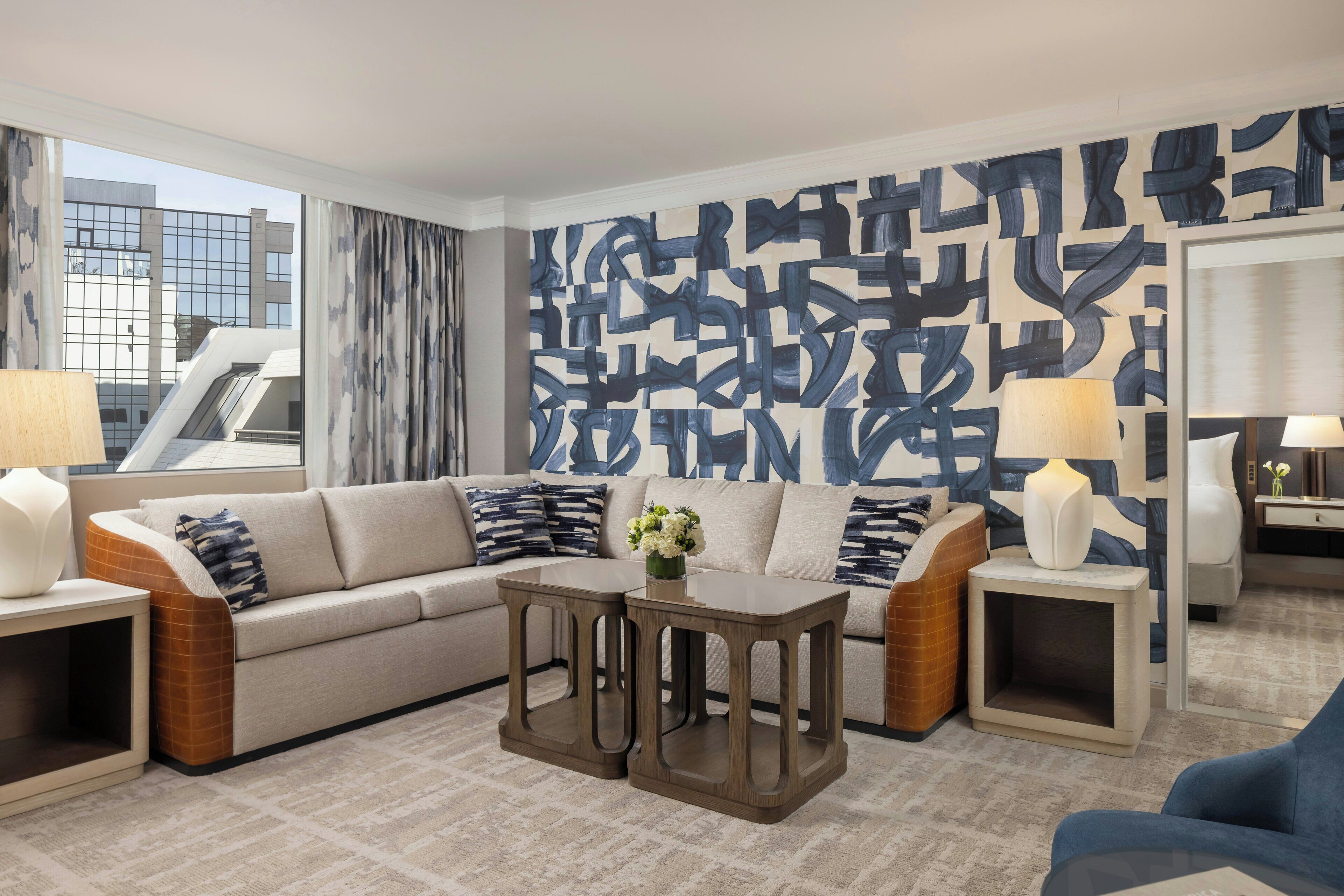 A modern living room with a sofa, two side tables, a coffee table, and a large abstract wall mural.
