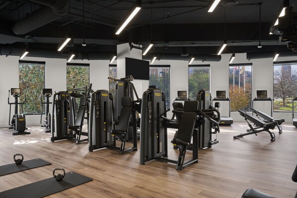 A gym with various exercise machines, wooden flooring, and large windows offering views of the outdoors. - Loews Nashville Hotel at Vanderbilt Plaza (Nashville)