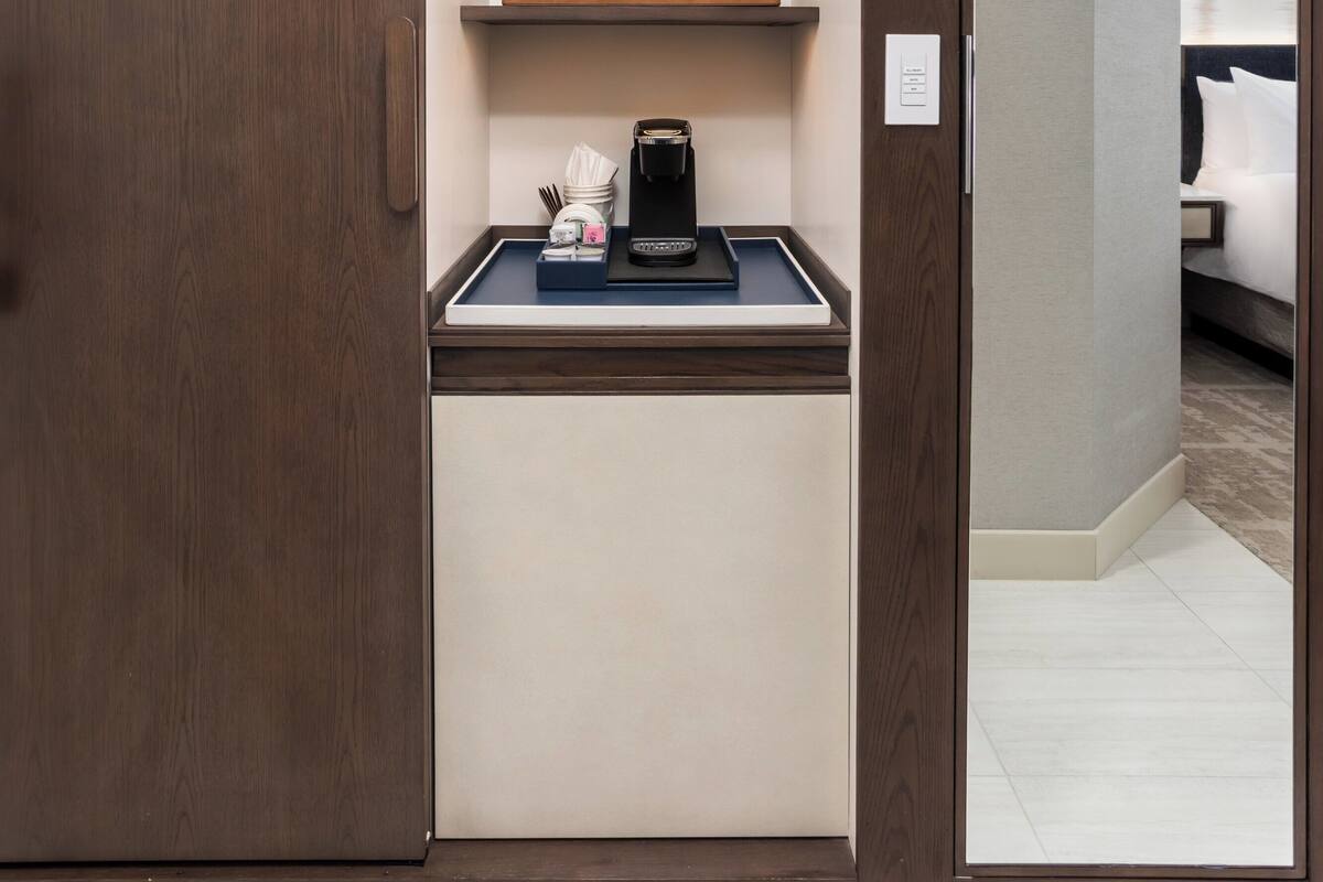A hotel room with a built-in kitchenette, a bed, and a bathroom visible through an open door.