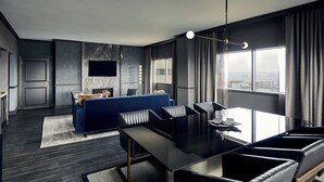 A modern hotel room with a dining area, a sofa, and a TV mounted on the wall.