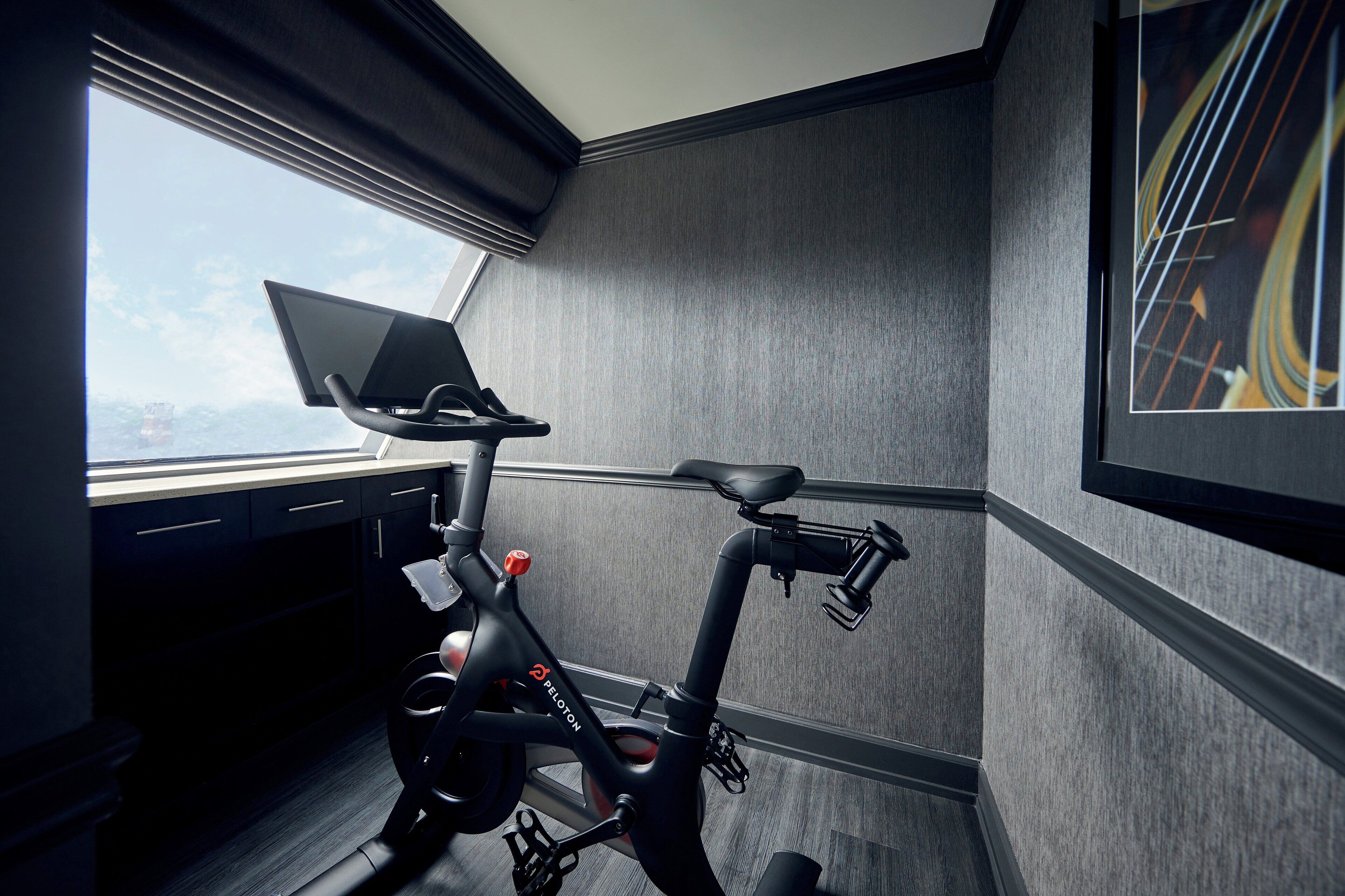 Una habitación moderna con una bicicleta estática, una ventana con cortinas y un cuadro enmarcado en la pared.