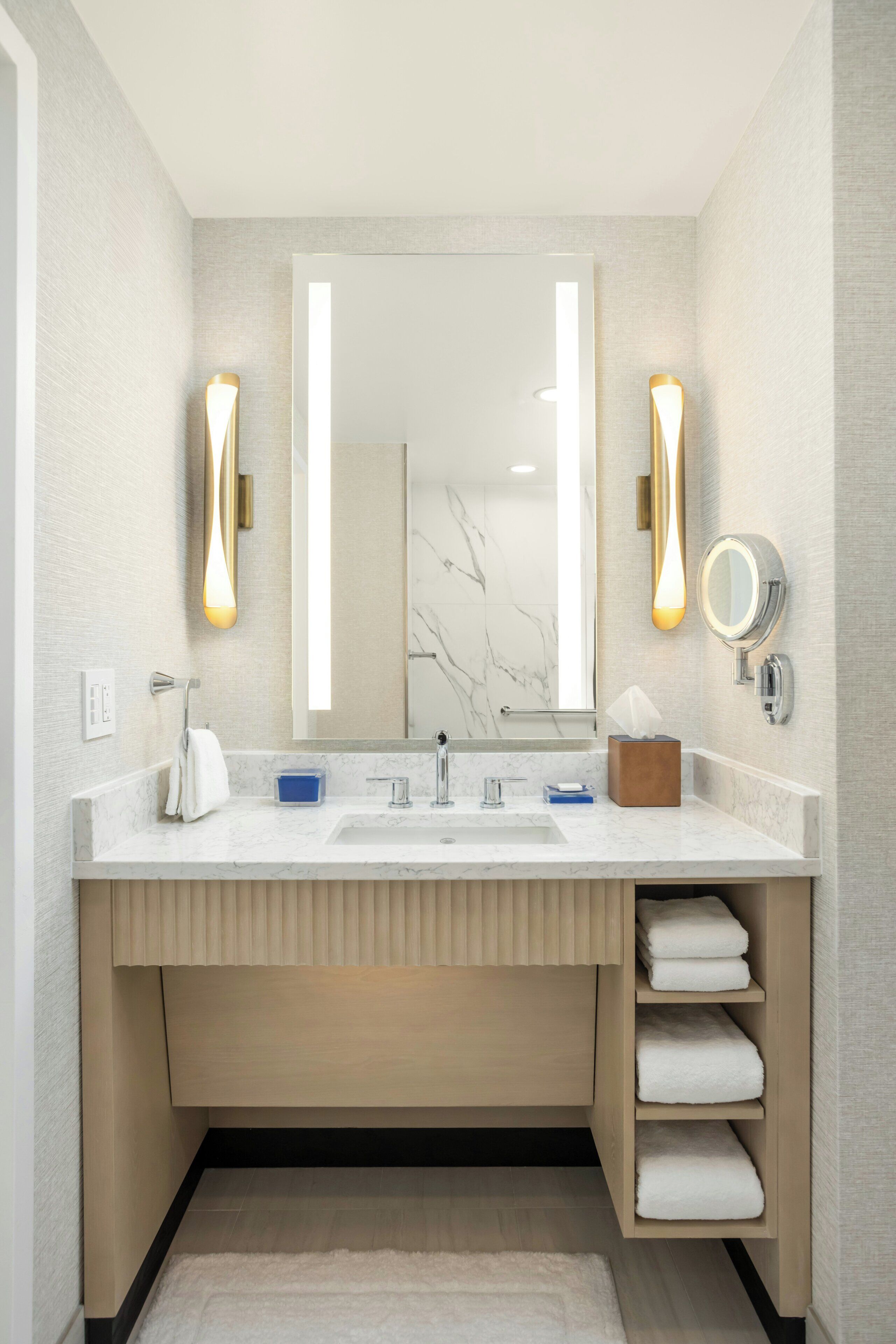 Une salle de bain moderne avec un grand miroir, deux appliques murales, un lavabo et un porte-serviettes.