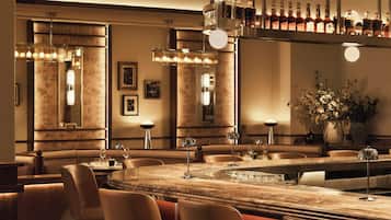 A bar area with a marble countertop, bar stools, and pendant lighting.