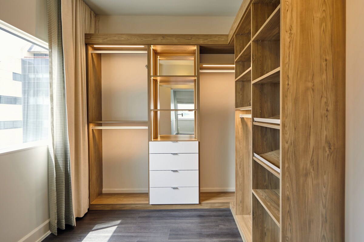 A walk-in closet with built-in shelves, a mirror, and a white dresser.