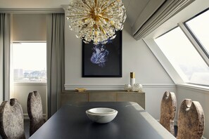 Un comedor moderno con una mesa oscura, un cuenco blanco y sillas originales. Un candelabro cuelga del techo, y una obra enmarcada adorna la pared.