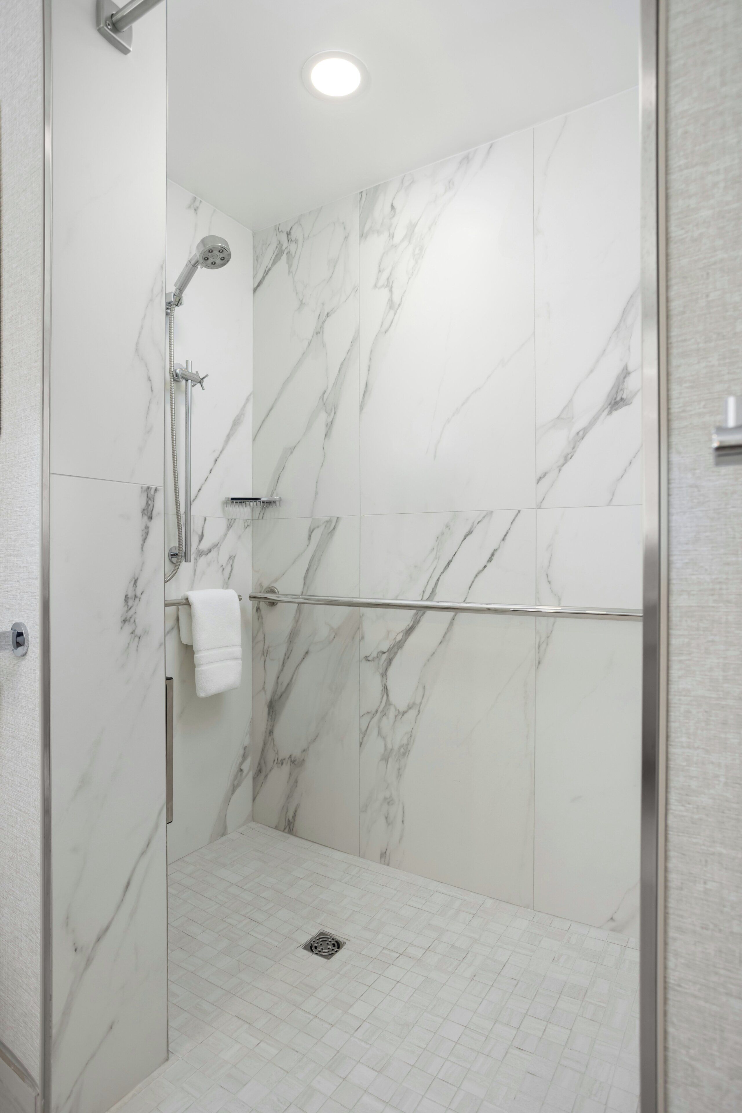 Une douche à l’italienne avec des murs en marbre et une porte en verre.