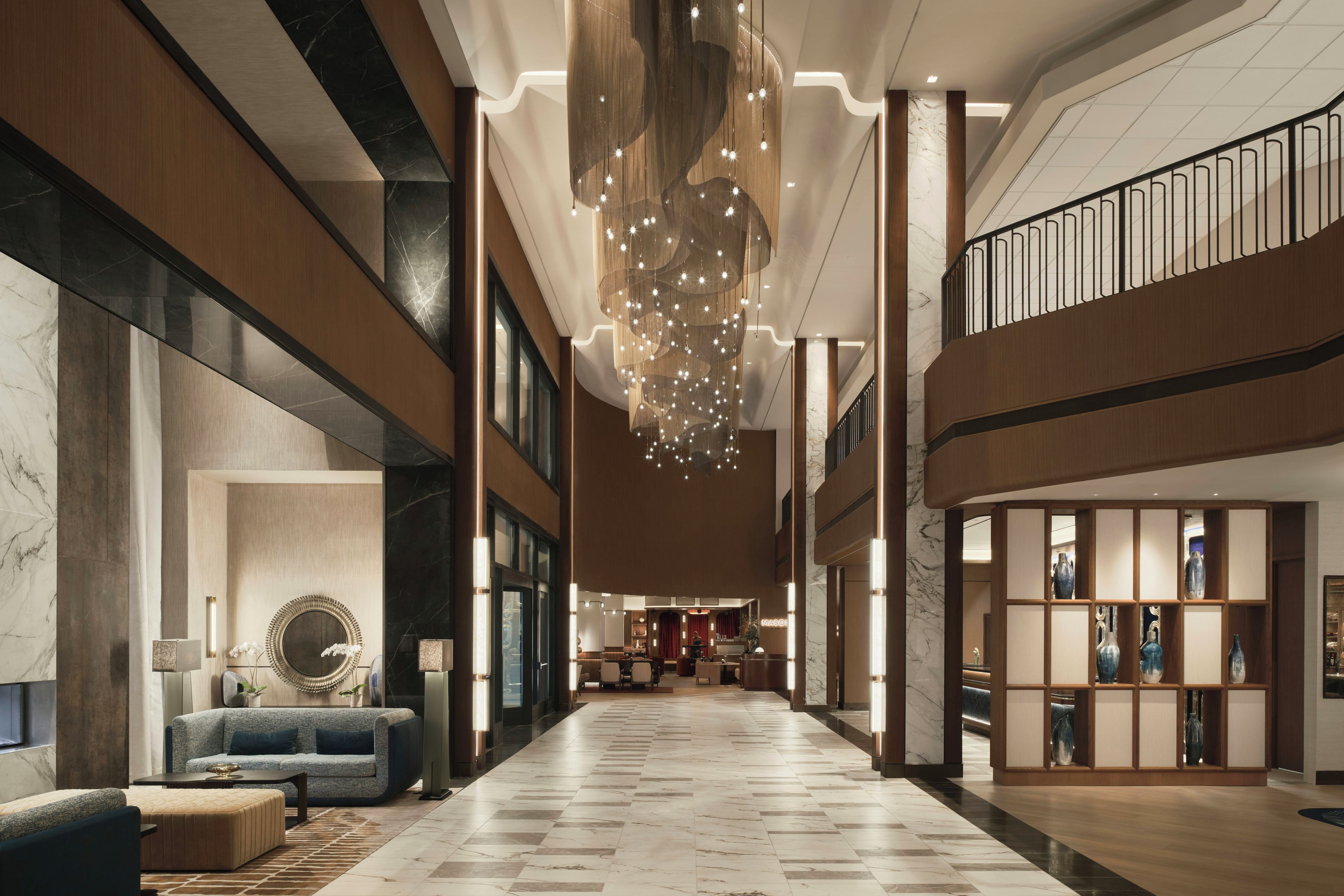 A spacious lobby with a high ceiling, a central chandelier, and a seating area with a sofa and armchairs.