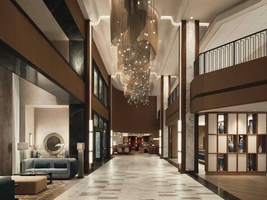A spacious lobby with a high ceiling, a central chandelier, and a seating area with a sofa and armchairs.