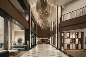 Un lobby espacioso con techo alto, un candelabro central y una zona de estar con sofá y sillones.