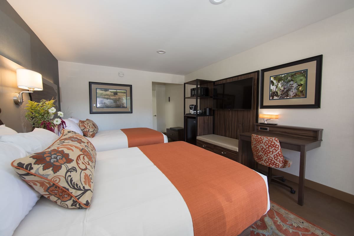 A hotel room with two beds, a desk, a chair, a TV, and a microwave.