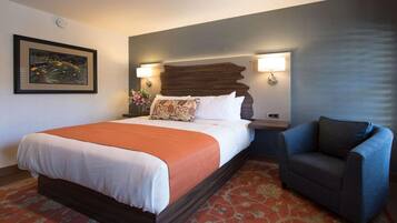 A hotel room with a large bed, a blue armchair, a decorative headboard, wall-mounted lamps, and a framed picture on the wall.