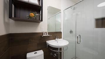 A modern bathroom with a white sink, a glass shower enclosure, and a wooden shelf above the sink.