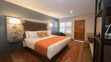 A bedroom with a large bed, a nightstand with a lamp, a chair, a desk, and a wardrobe.