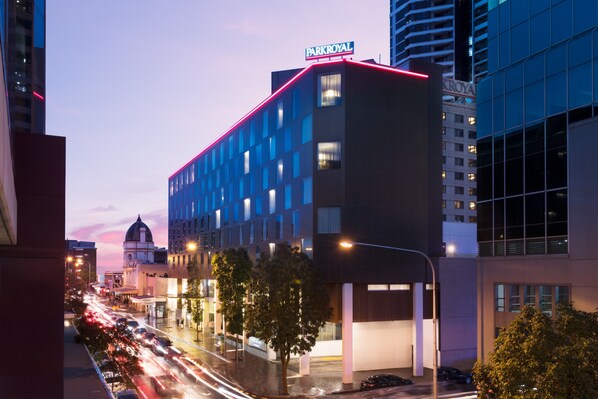 A modern hotel with a prominent sign, a parking garage, and a busy street with light trails.
