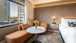 A modern hotel room with a sofa, a round table, a bed, and a view of the cityscape. - PARKROYAL Parramatta (Parramatta)