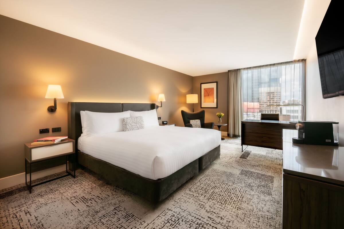 Ein Hotelzimmer mit einem großen Bett, Nachttischen, einem Schreibtisch und einem Fernseher.