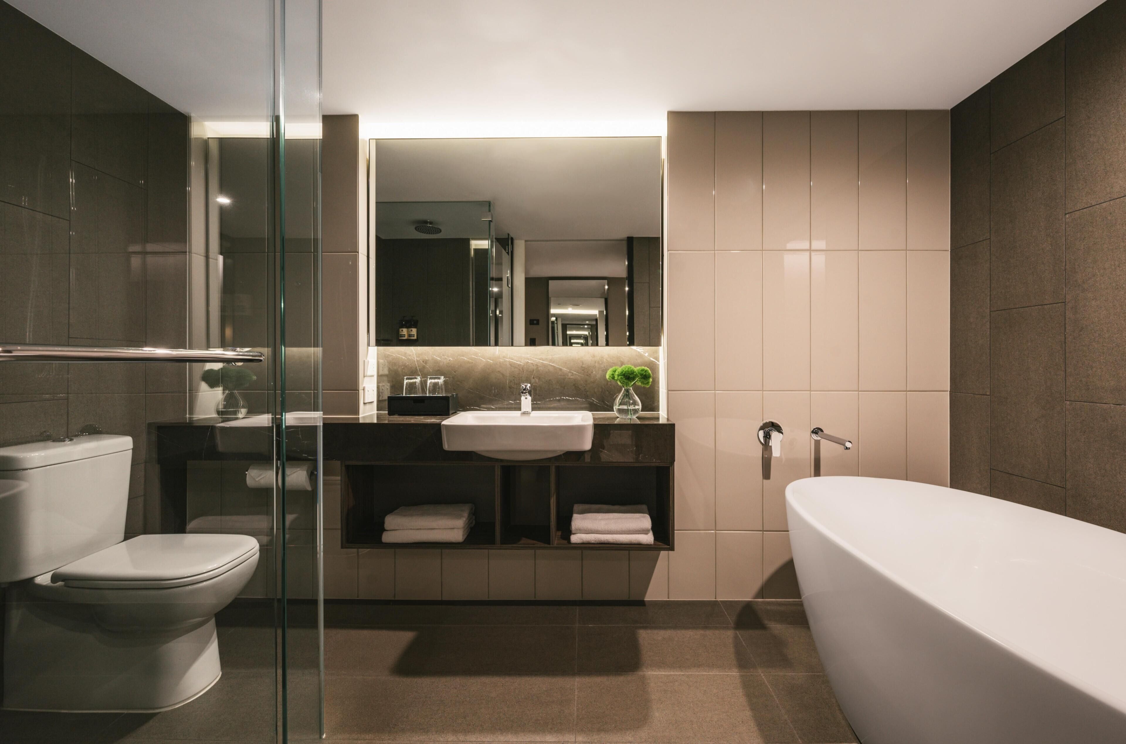 A modern bathroom with a glass-enclosed shower, a white toilet, a sink with a mirror above, and a freestanding bathtub.