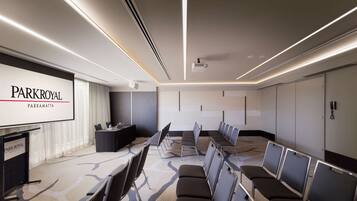 Una sala de conferències amb una pantalla gran que mostra 'PARKROYAL PARRAMATTA', una fila de cadires, una taula amb un ordinador portàtil i un projector al sostre.