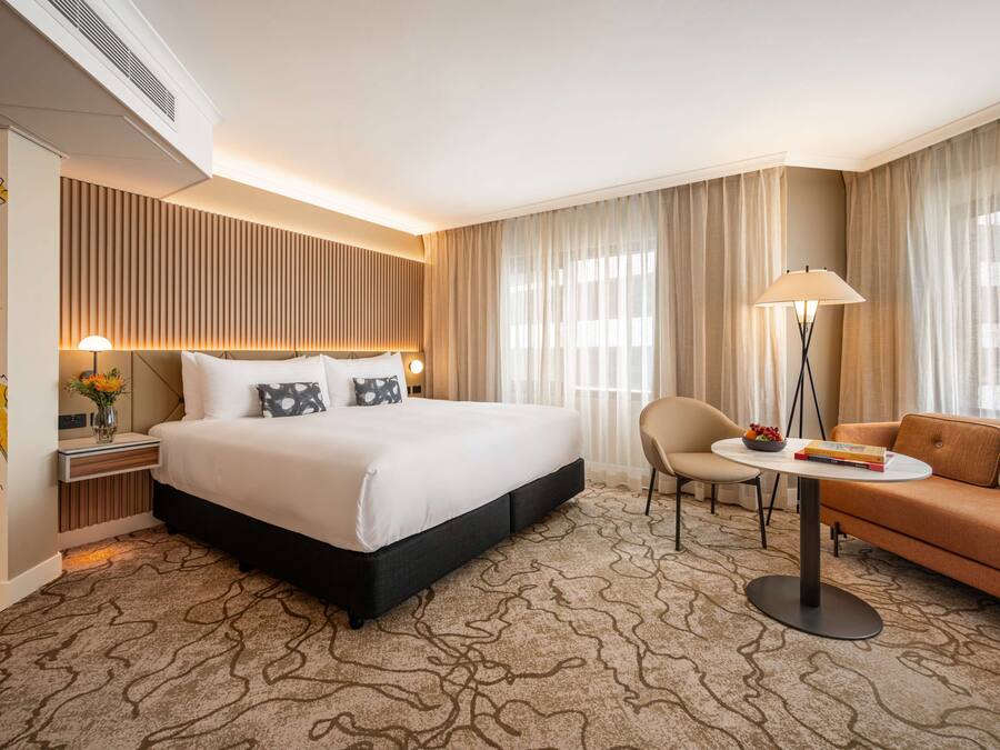 A hotel room with a large bed, a sofa, a small table, and a lamp.